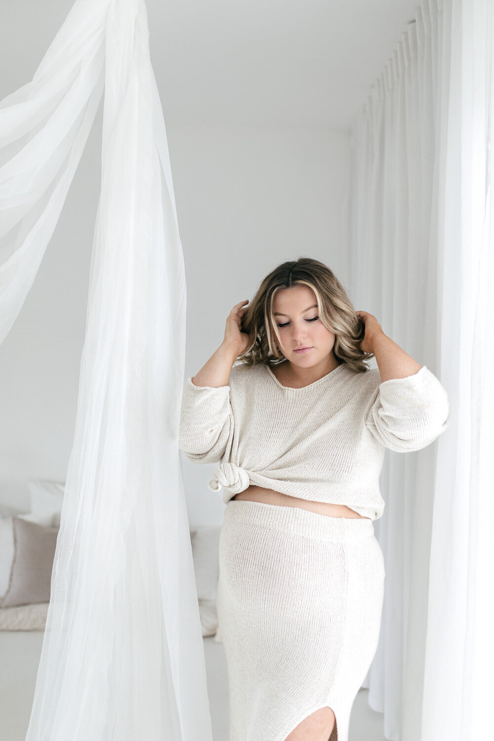 Pregnany women wearing beige clothng reaches up to tuck her hair back behind her ears