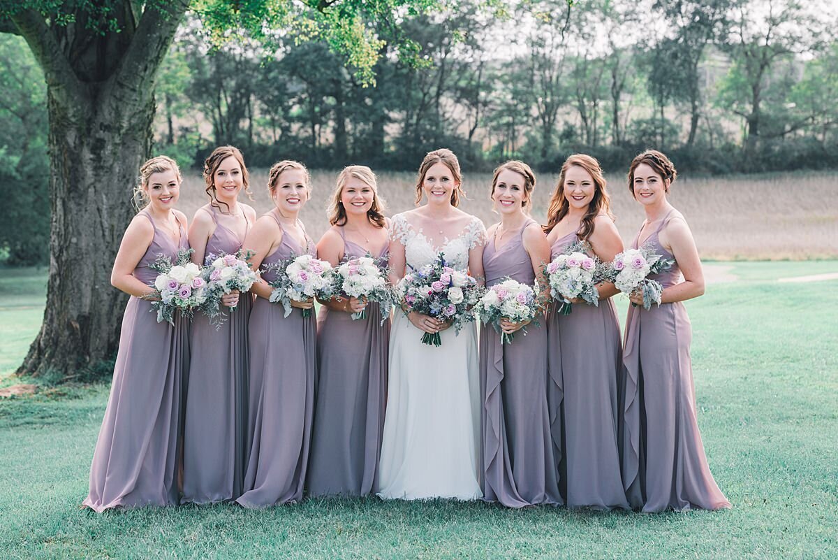 Bridesmaids dressed in dusty purple dresses stand on either side of the bride holding white bouquets at Rippavilla Plantation