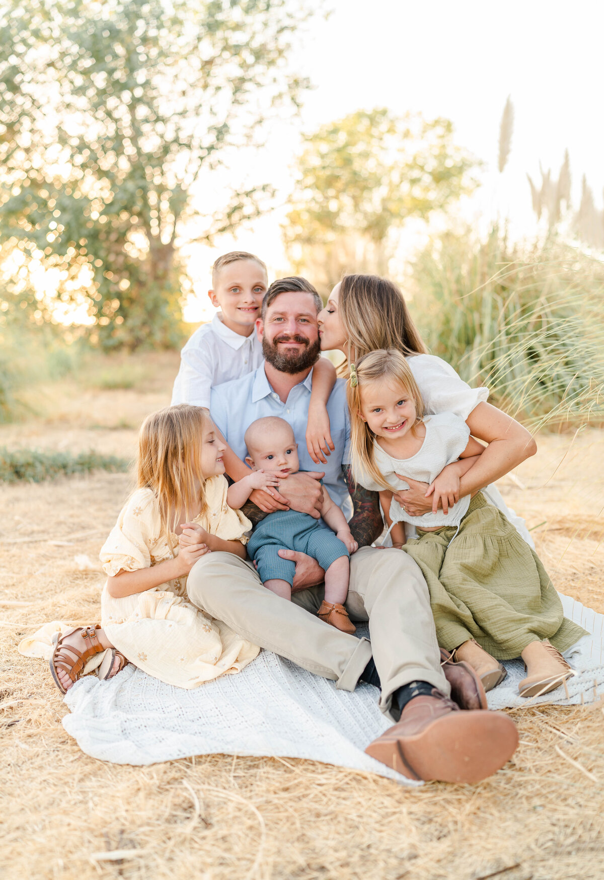A family sits together lovingly in a pampas grass field dressed in muted tones of yellows, tans, and greens photographed by Bay Area Photographer, Light Livin Photography.