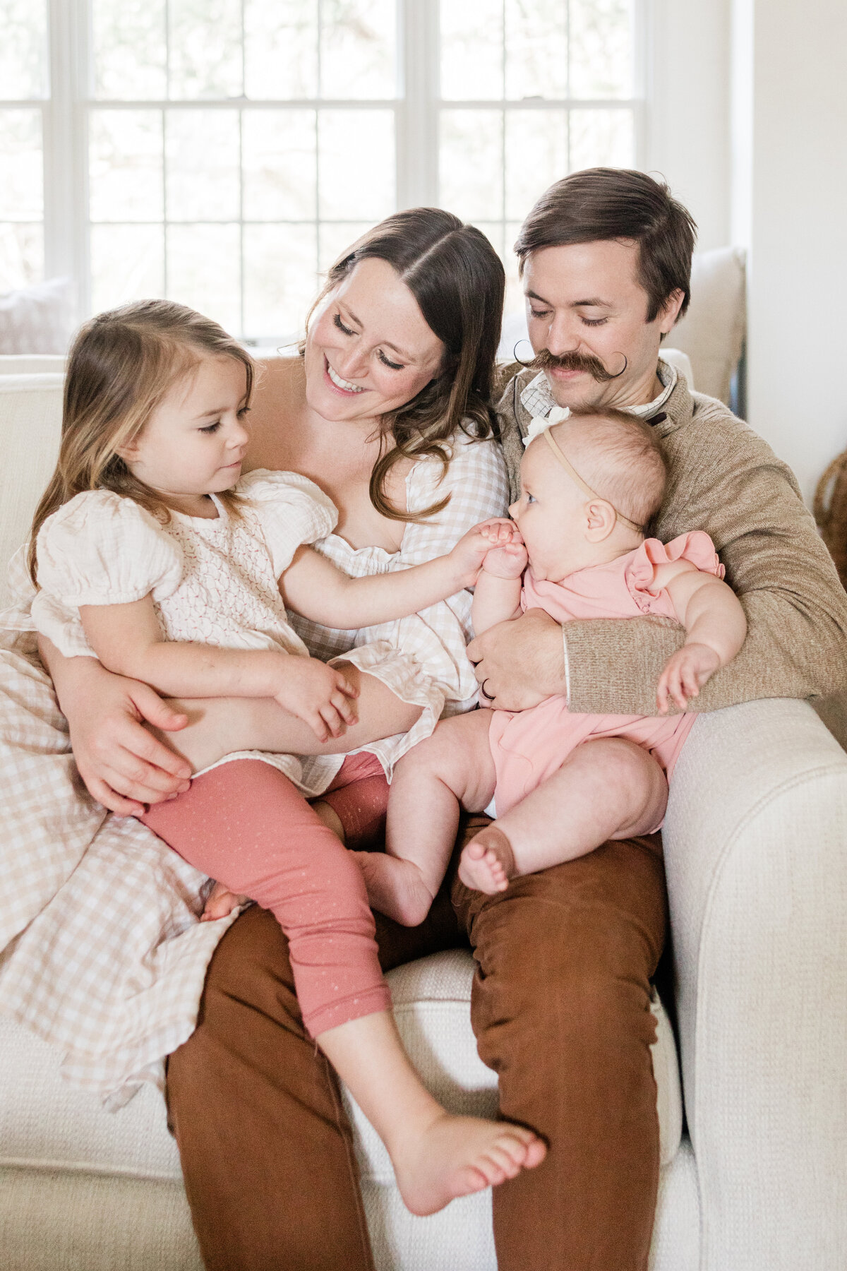 Parents snuggling on couch with their two young daughters