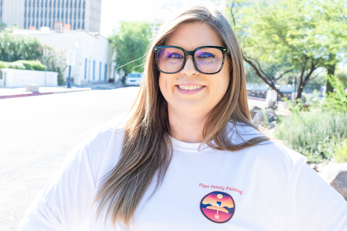 Confident woman in a white shirt and glasses posing outdoors on a sunny day, photographed by Vyrl Photo, showcasing Tucson brand photography.