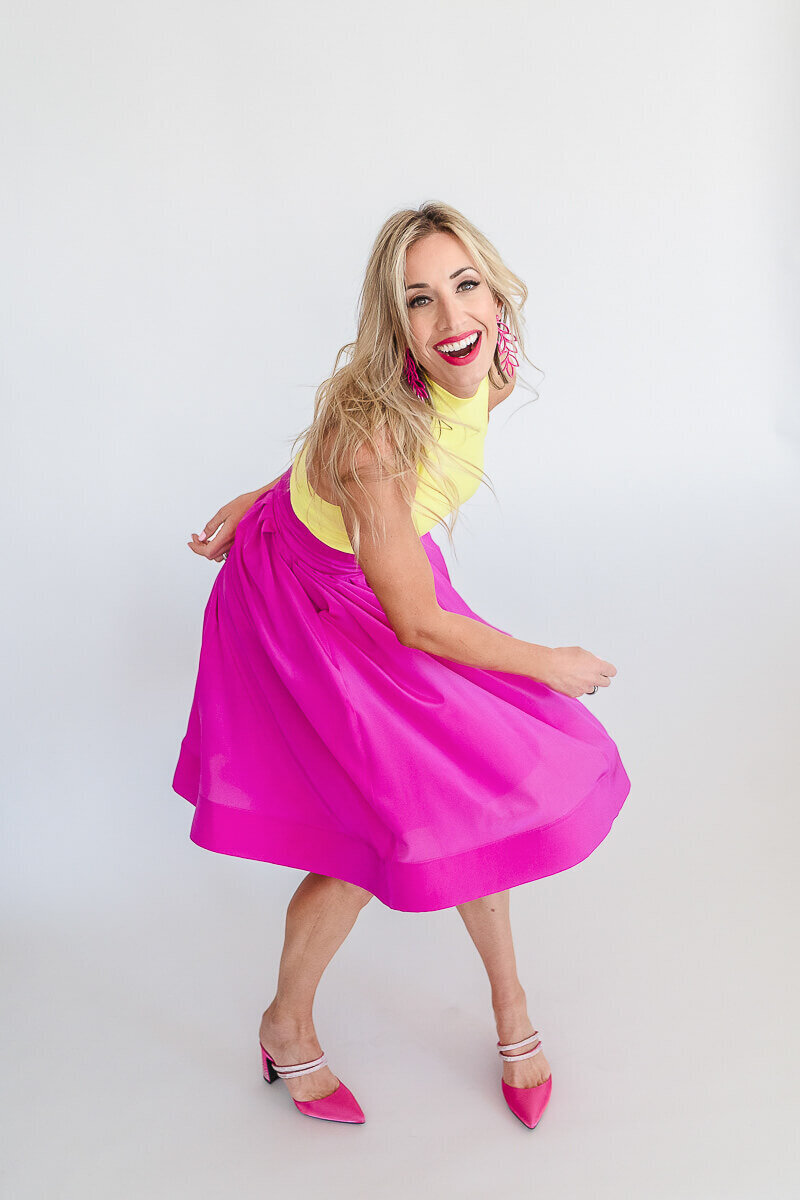 Woman mid-twirl in a pink skirt with a bright yellow sleeveless top, hair moving with the spin.