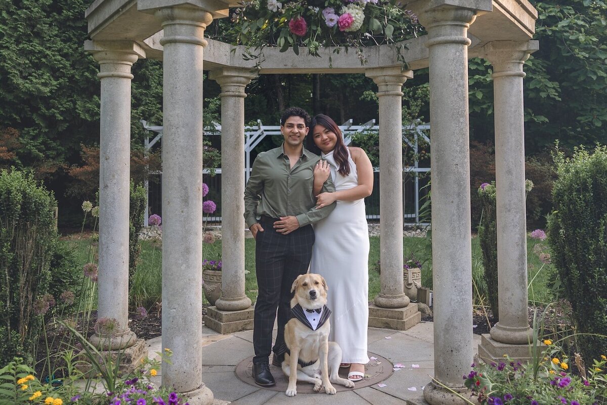 Couple standing under pergola with their dog for a sweet family photo.