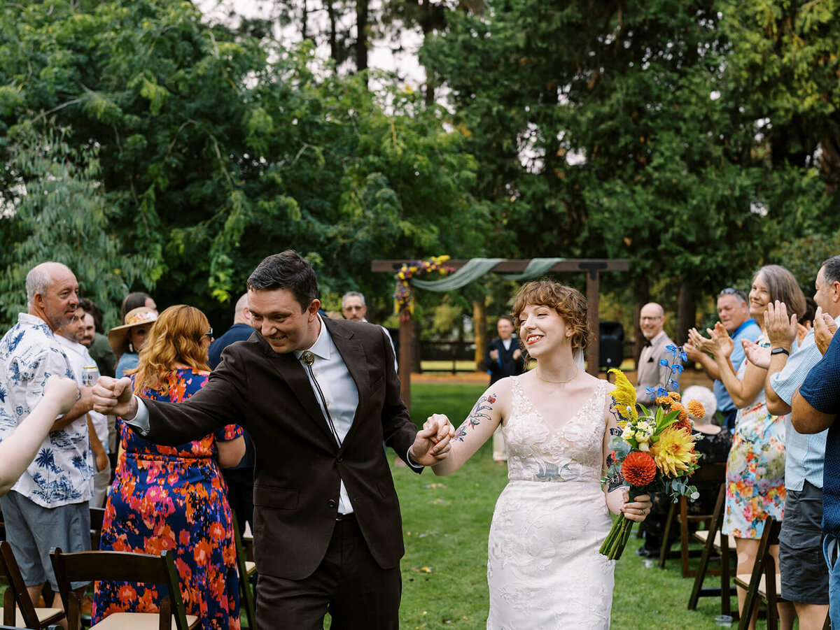 Bride and groom happy in the aisle as the groom fist bumps a guest. 