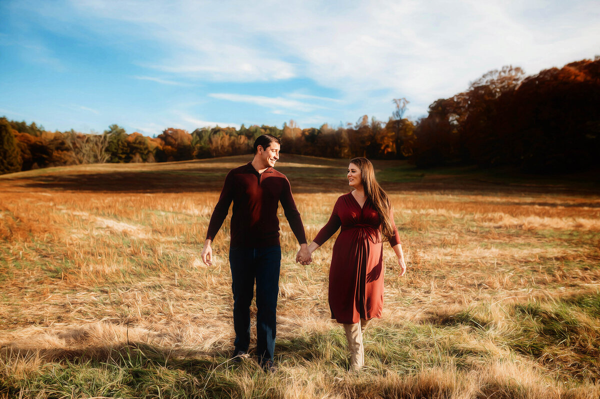 Expectant parents walk together in a field during Maternity Portrait Session at Biltmore Estate in Asheville, NC.