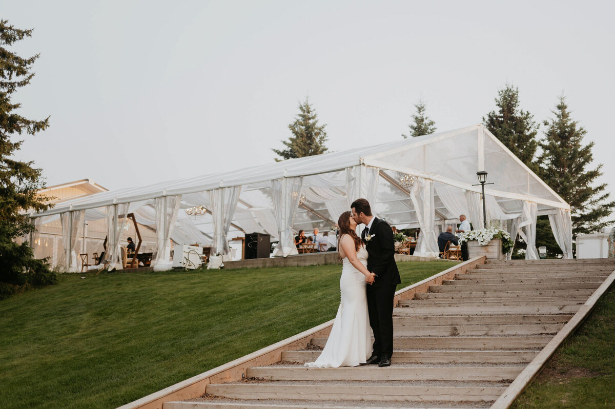 Bride and groom on the stairs at Pine & Pond, a natural picturesque wedding venue in Ponoka, AB, featured on the Brontë Bride Vendor Guide.