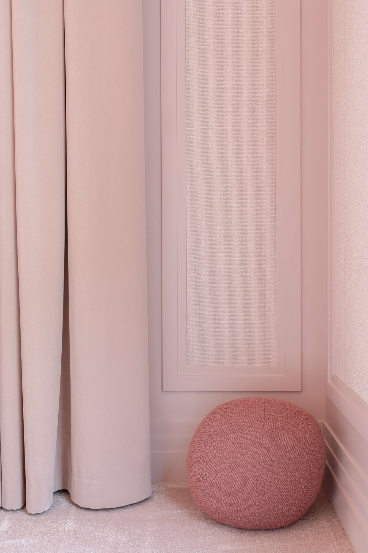 Pink drapes against a light pink wall in a girl's bedroom. There is a sphere ottoman in a deeper pink in the corner.