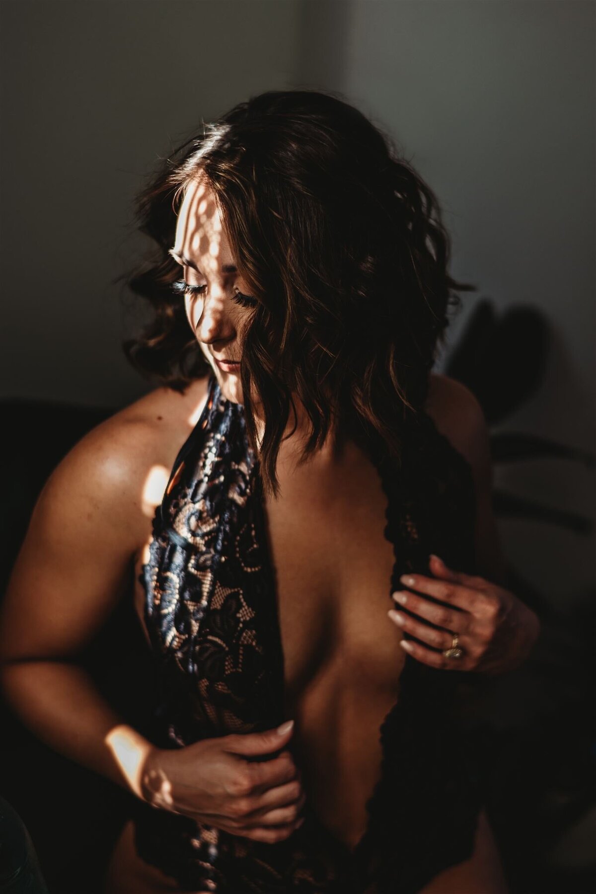Baltimore photographers  captures boudoir pictures with woman in a one piece lingerie while holding her hands on her outfit while looking over her shoulder