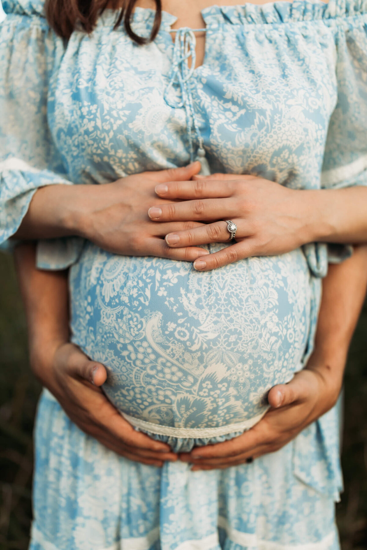 Mother and father placing hands on baby belly with mom in blue maternity dress.