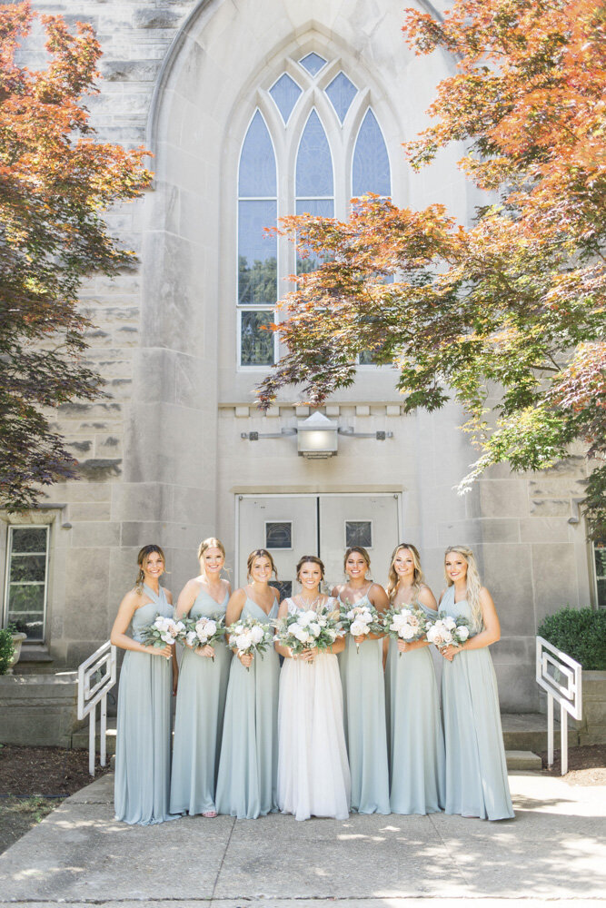 Bride and her bridesmaids standing outside church on fall wedding day in Terre Haute