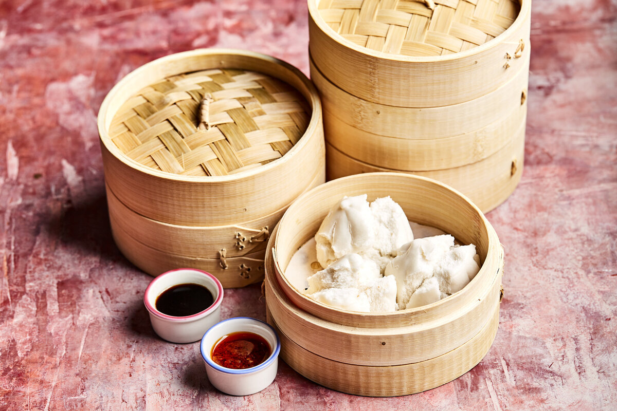 Dumpling steaming baskets stacked up with two different dipping sauces next to them.