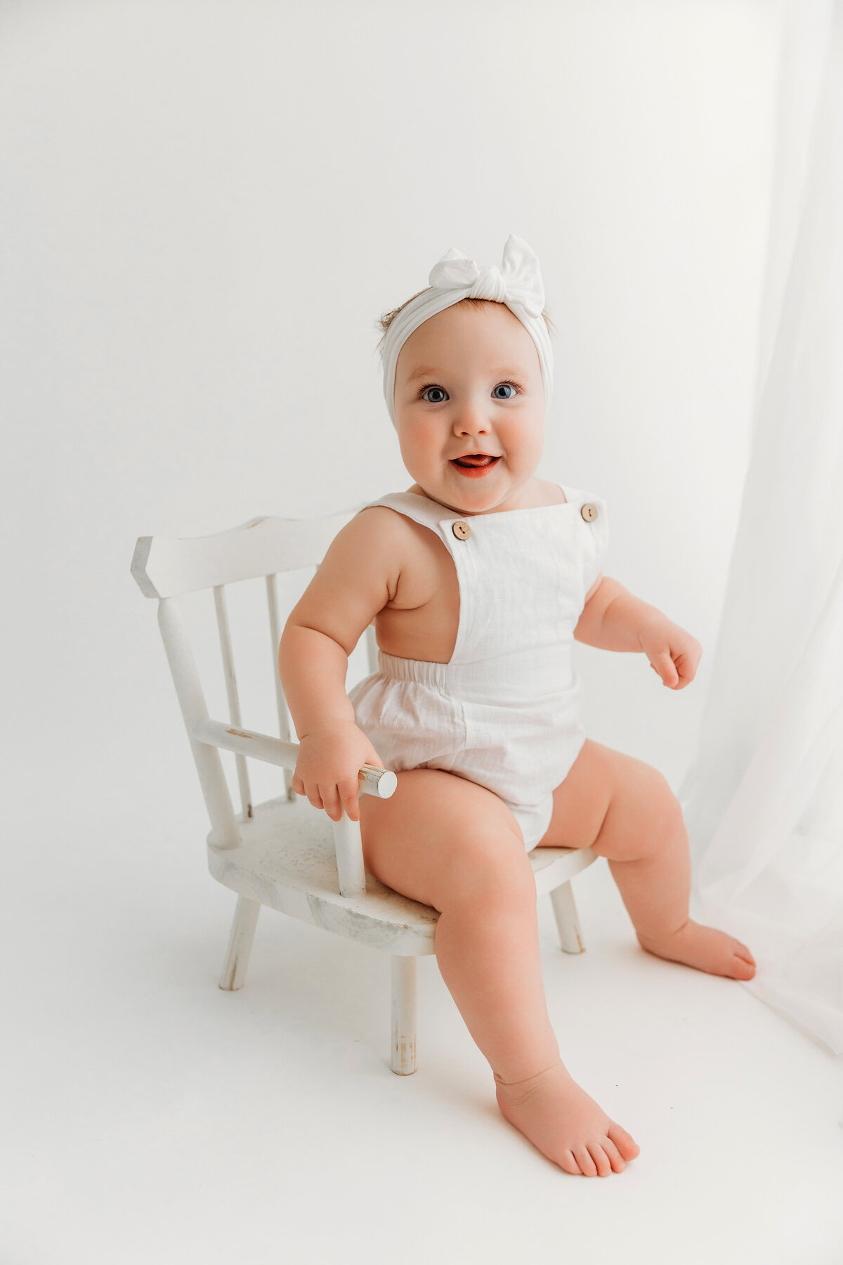 baby girl smiling on white chair for portraits in phoenix