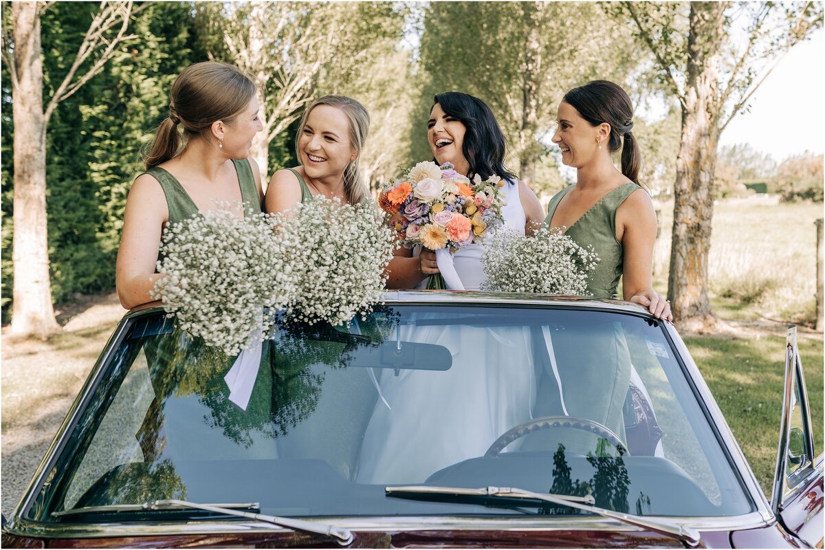 bride and bridesmaids in convertible car with gypsophila bouquet and green dresses private venue christchurch for wedding laughing