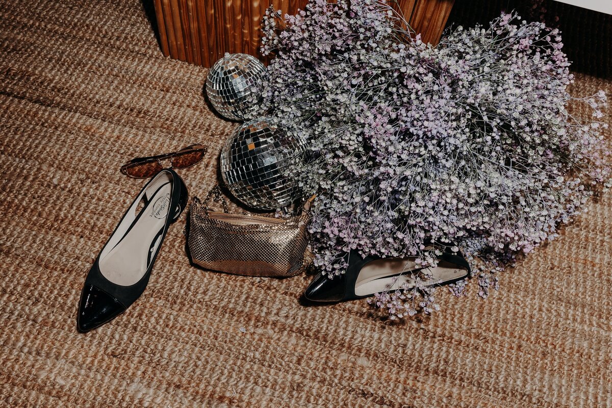 Shiny purse and pair of black heels left near disco balls and babys breath at wedding reception