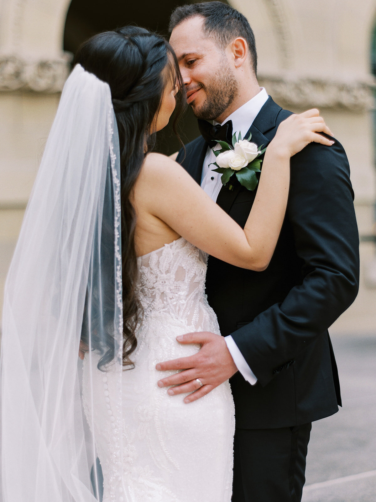 A bride and groom embrace on their wedding day at the Fairmont Palliser in Calgary, with the bride wearing a white dress and veil and the groom in a black suit. They stand closely while gently touching heads, creating a timeless memory of their cultural Calgary wedding.