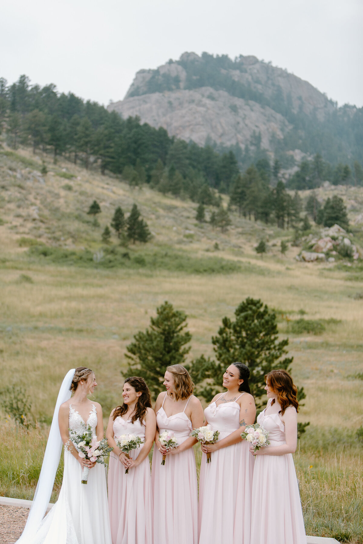 A bride and her bridesmaids smile at eachother in Lory State Park, Colorado.