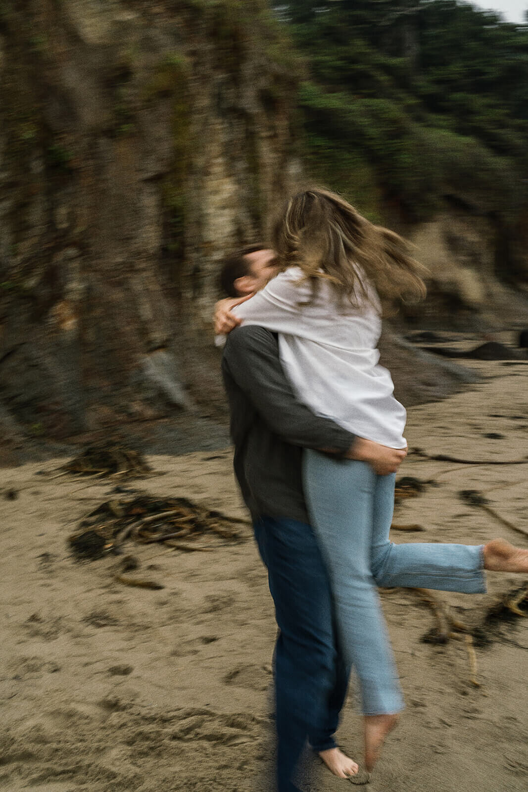 Blurry capture of a man lifting a woman in his arms to embrace with rocks and sand behind them. 