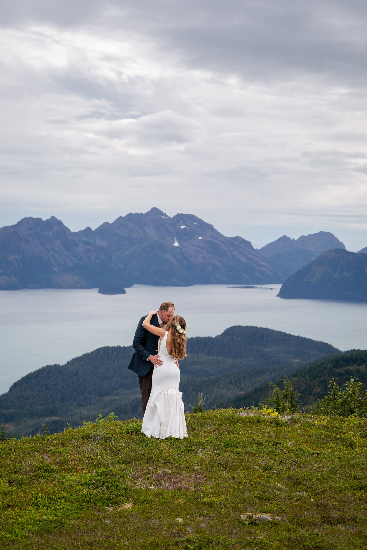 A bride and groom dance on top of a green hill overlooking a bay.