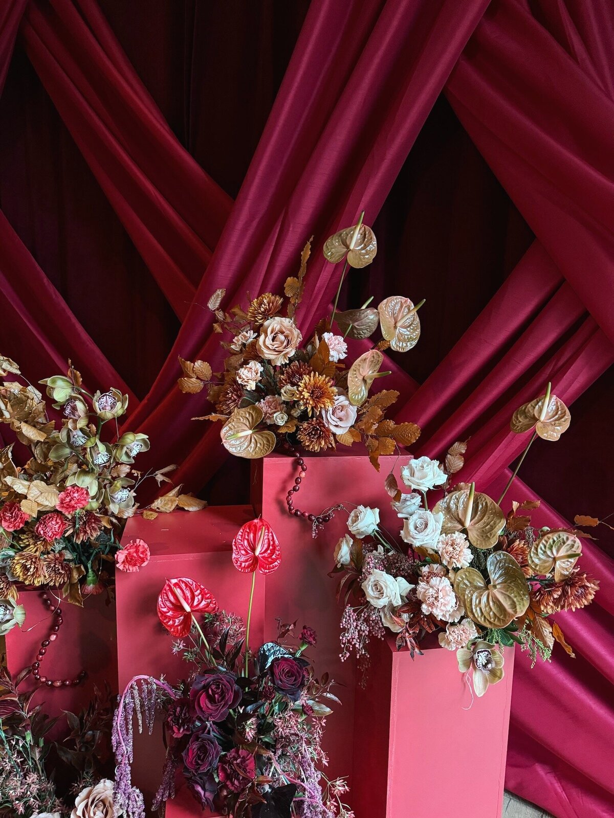 Bold photo moment with floral columns for corporate event entrance. Red carpet entrance for corporate gala. Floral design with color gradients of copper, burgundy, red, blush, and cream. Sculptural floral arrangements for large scale floral installation. Winter event florals with unique and bold design. Design by Rosemary & Finch Floral Design in Nashville, TN.