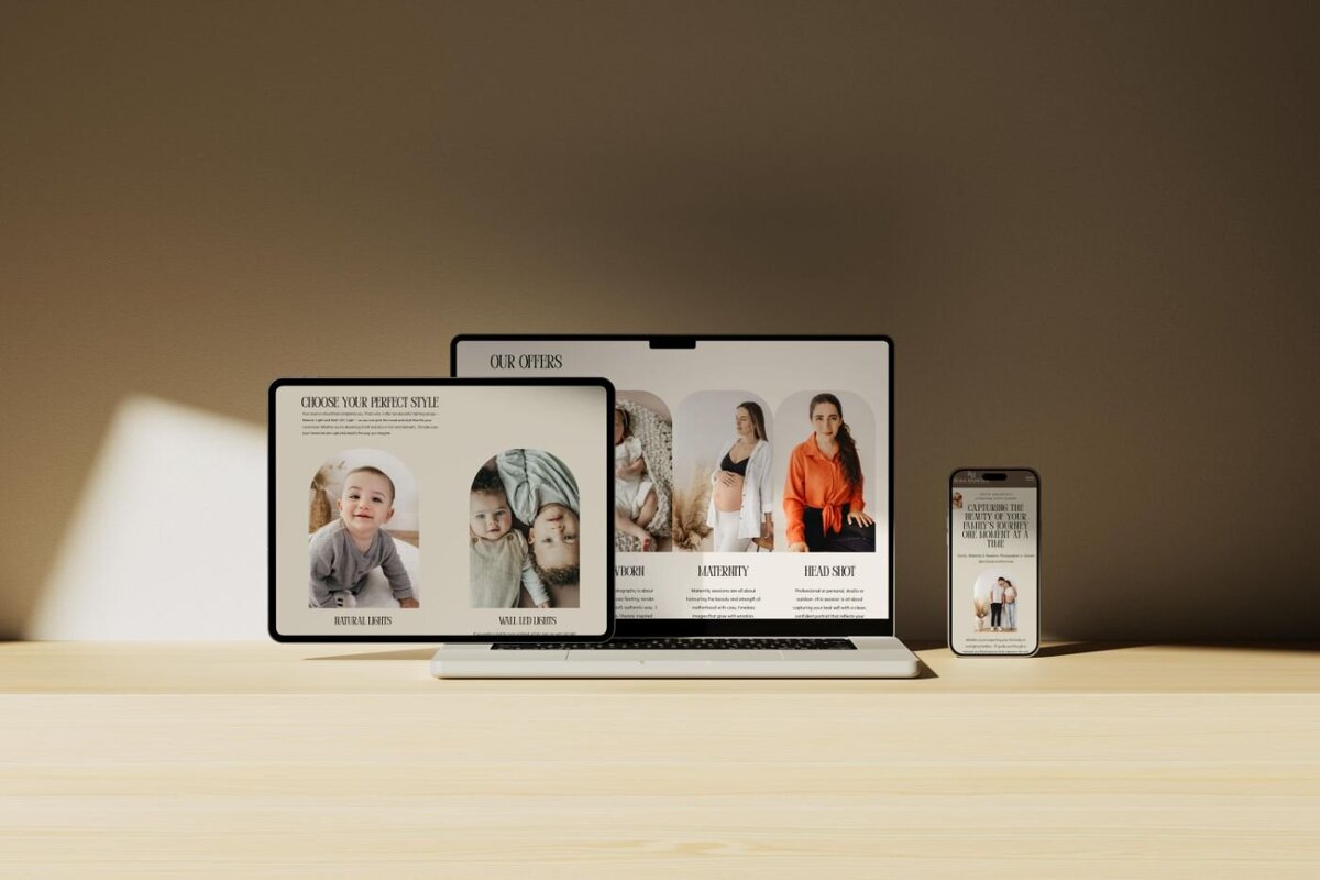Collection of devices on a wooden table—a tablet, laptop, and smartphone—all displaying different pages of a photography website with newborn portraits, maternity and headshot offers in warm natural light.