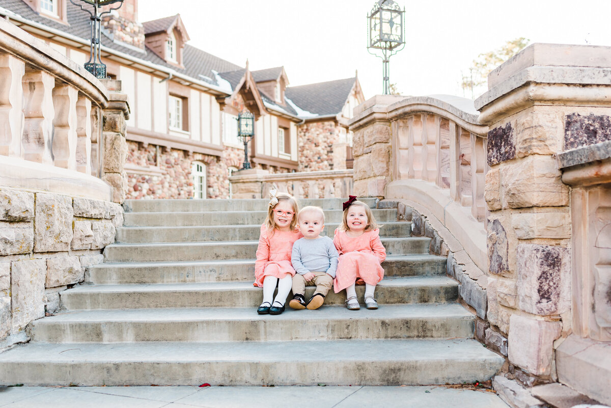 colorado wedding photographers captures her three toddler children sitting together on a set of stone stairs outside of a large beautiful building for denver family photos