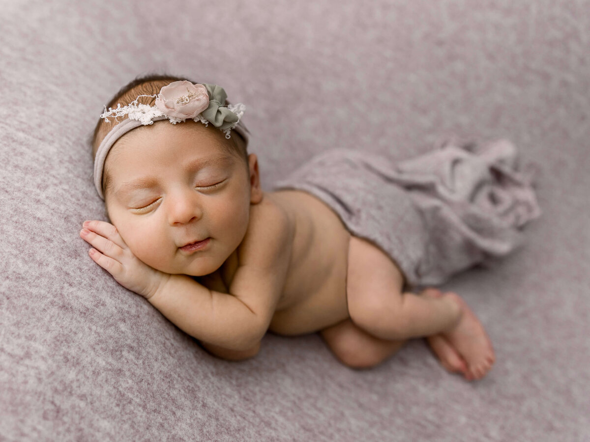 Newborn girl in a side laying pose on a mauve backdrop in an Erie Pa photography studio