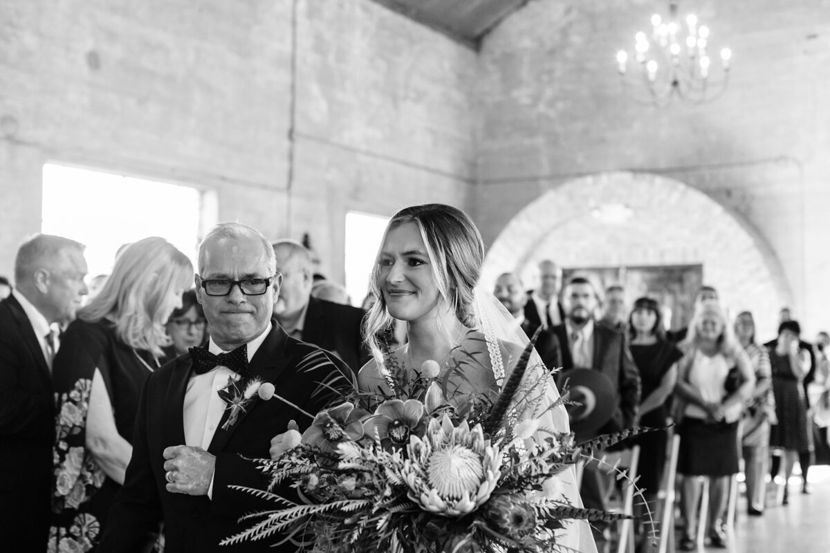 Emotional black and white photo of bride and her father walking down the aisle and seeing her groom for the first time at Olde Dobbin Station.