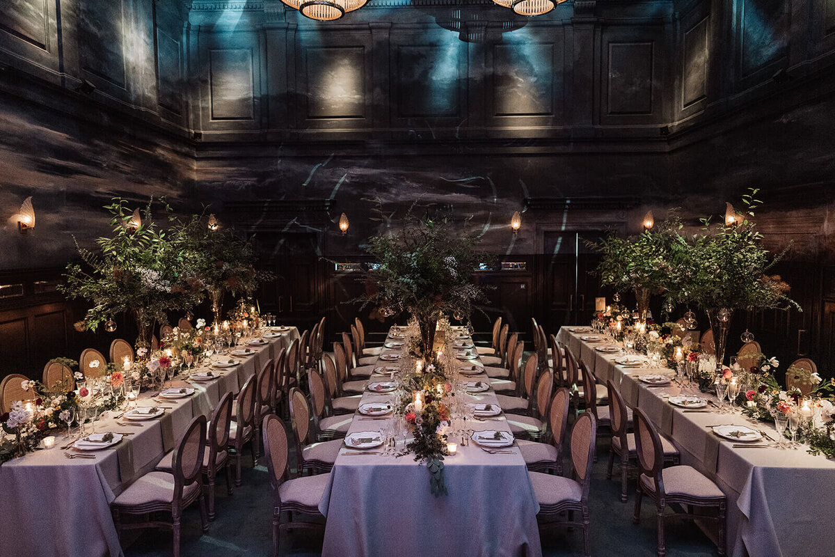 three long candlelit dining tables set up in the nomad london’s ballroom with trees as table decoration for an intimate wedding celebration