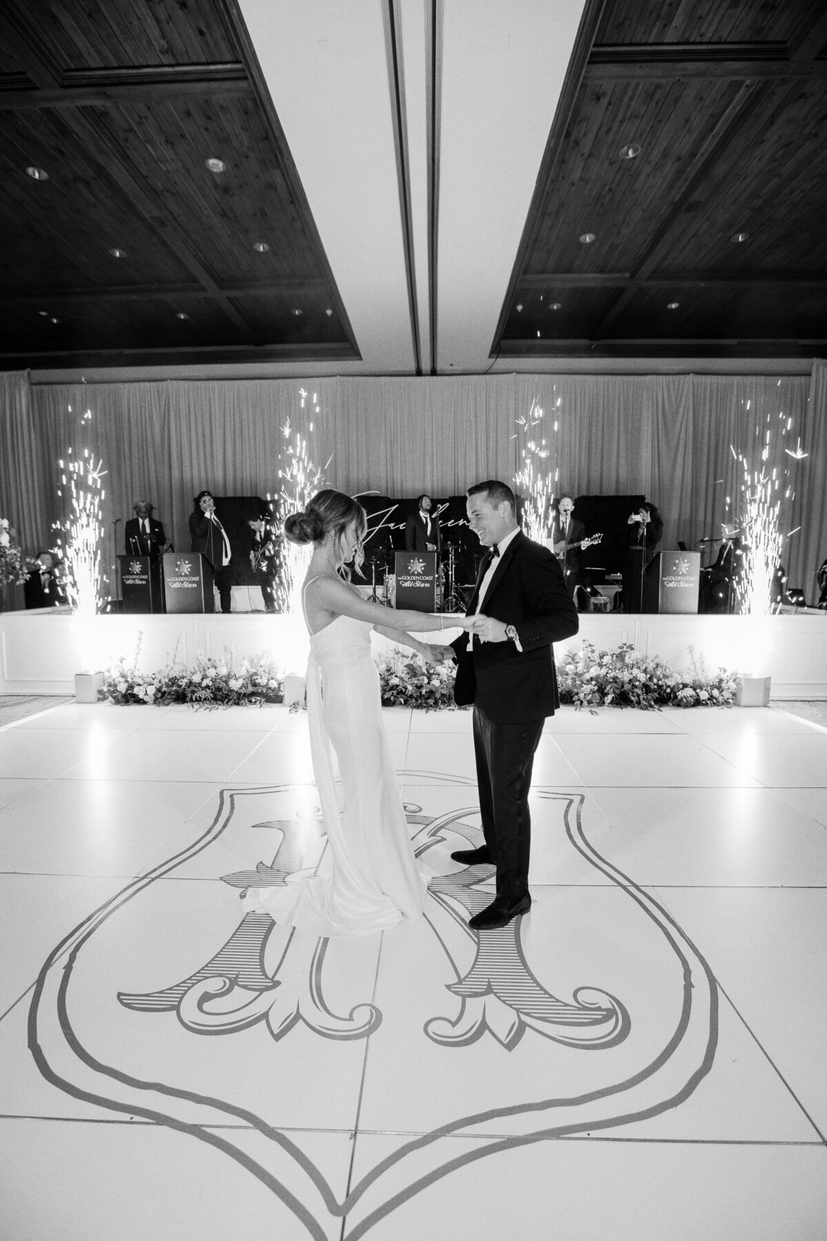 A timeless black and white wedding photo capturing the bride and groom’s first dance, with sparkling fireworks and live music in the background.