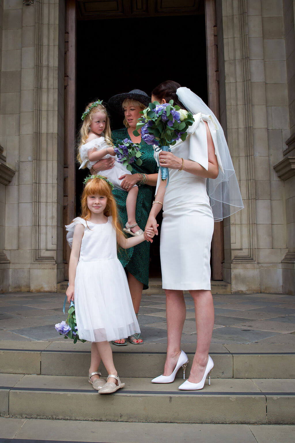 Bride and brides party posing on steps of Brompton Oratory.  Only little girl looking to camera