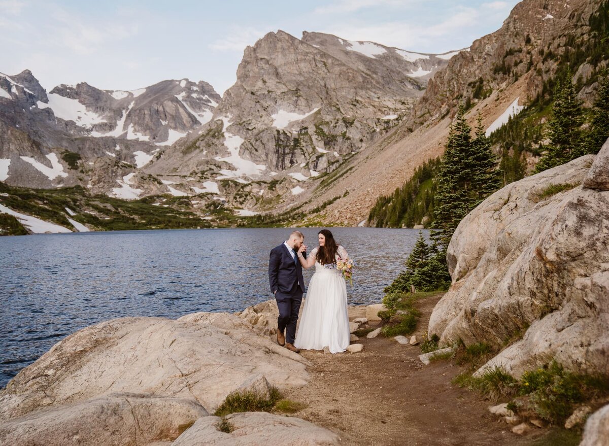 Couple walks hand in hand on the shore of Lake Isabelle for their Colorado elopement as groom kisses the brides hand