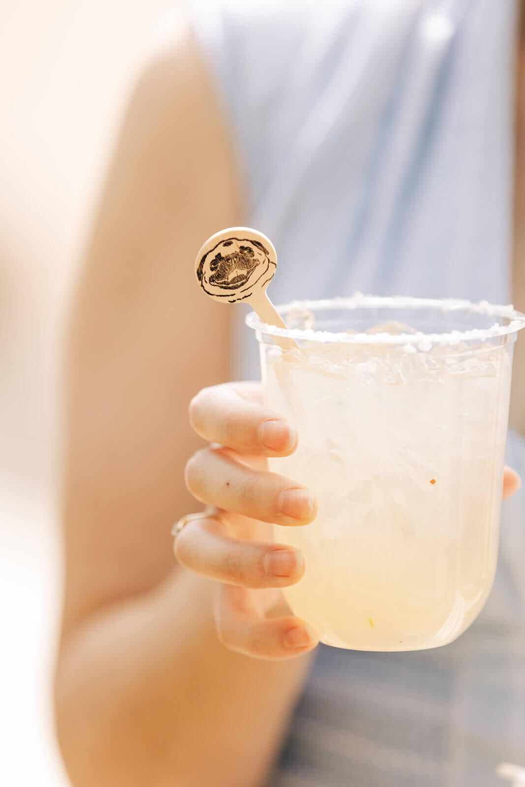 A woman's hand holding a drink with a wooden stir stick featuring a dogs face, representing wedding details planned by Perfect Thirds and CO. 