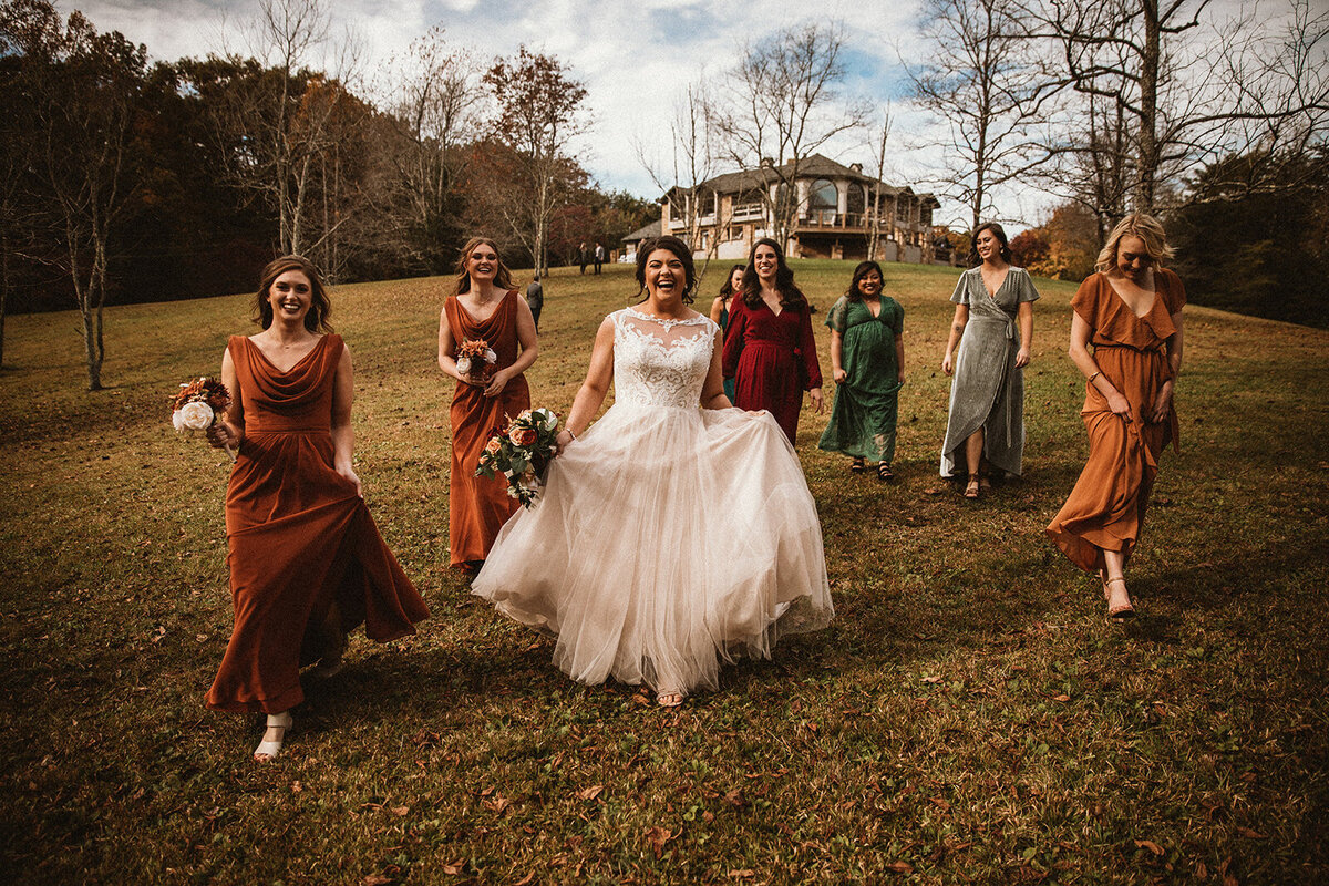 bride walks in a field with bridesmaids wearing multiple fall colors