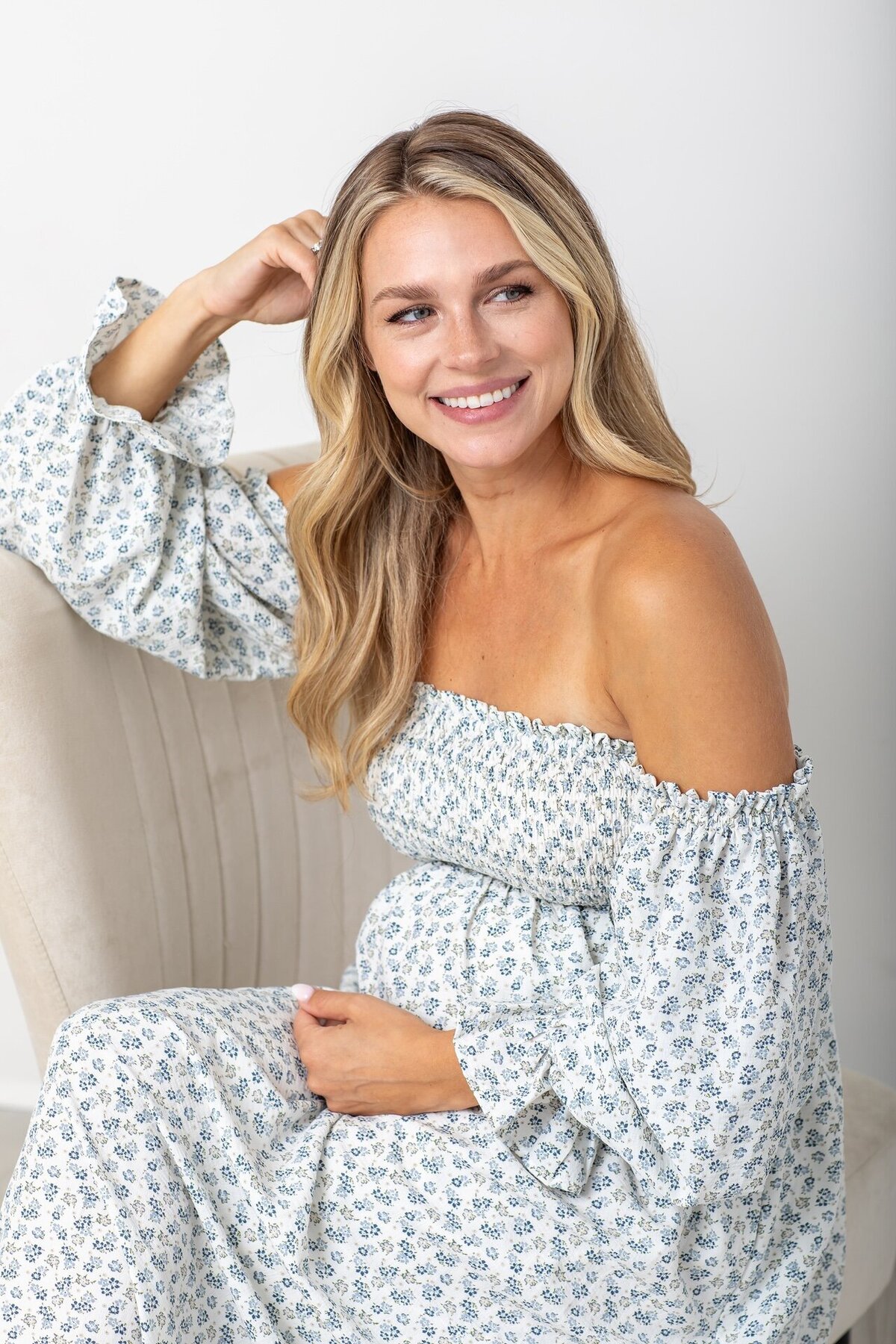 Pregnant mom-to-be sitting and smiling in a soft white and blue dress
