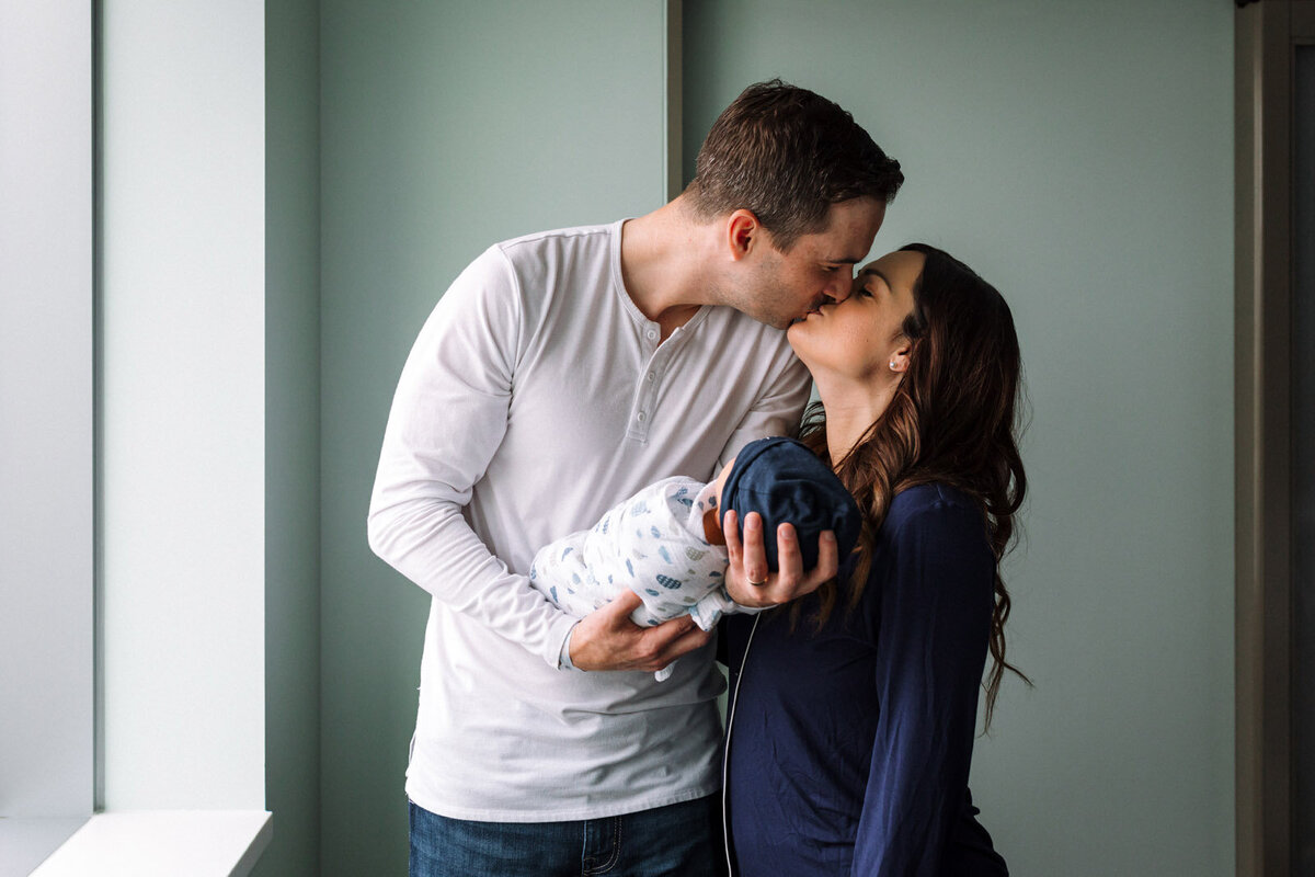 parents kissing in hospital while dad holds newborn