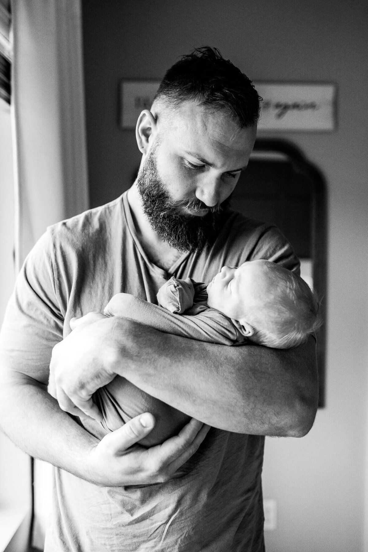 Black and white image of a father holding his newborn son by window. Photo by Portland Oregon newborn photographer.