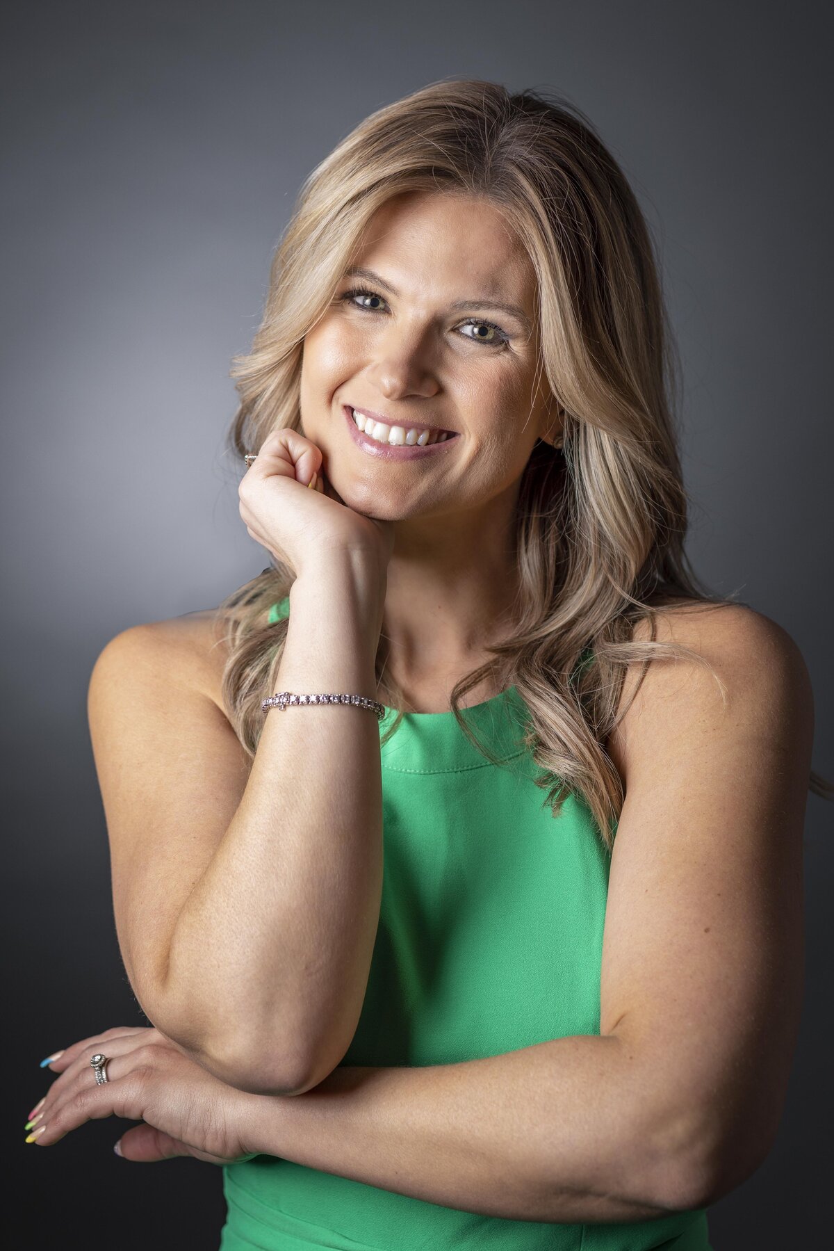 Professional headshot in CT of smiling woman in green sleeveless top, leaning on hand by Rob Faber Photography.