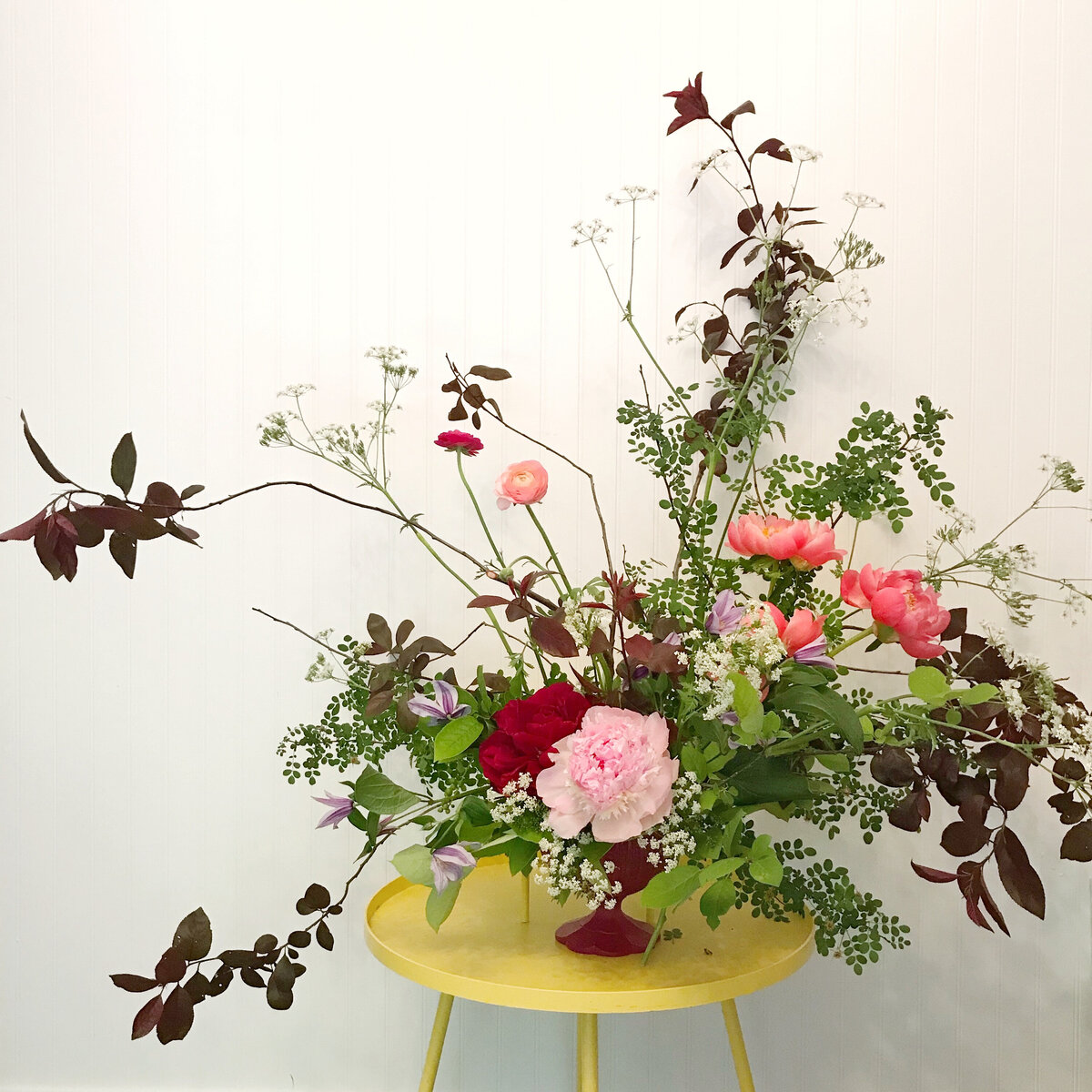A lush, airy arrangement of spring flowers sitting on a yellow stool.