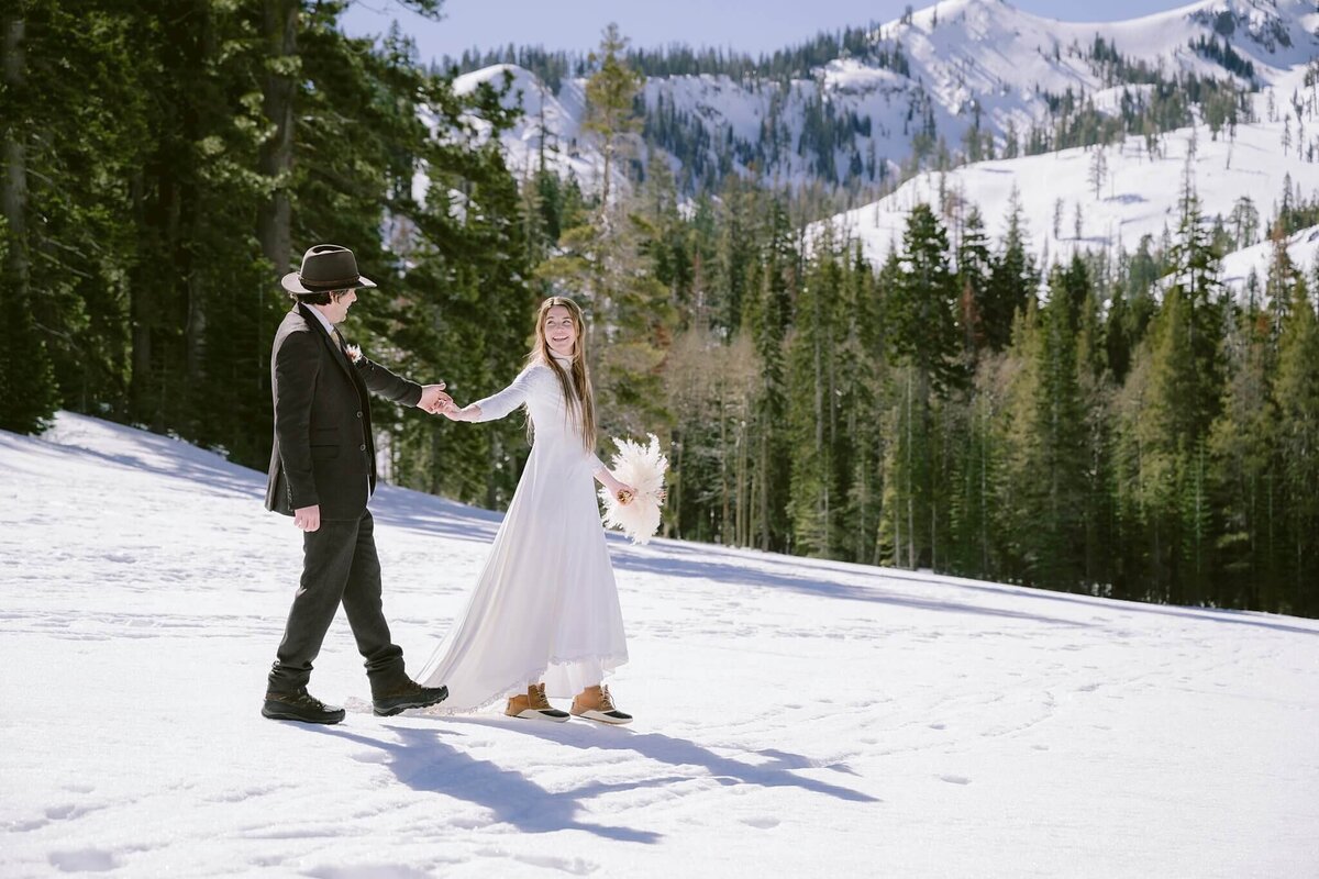 Bride and groom holding hands during elopement during winter in Palisades Tahoe with mountain backdrop