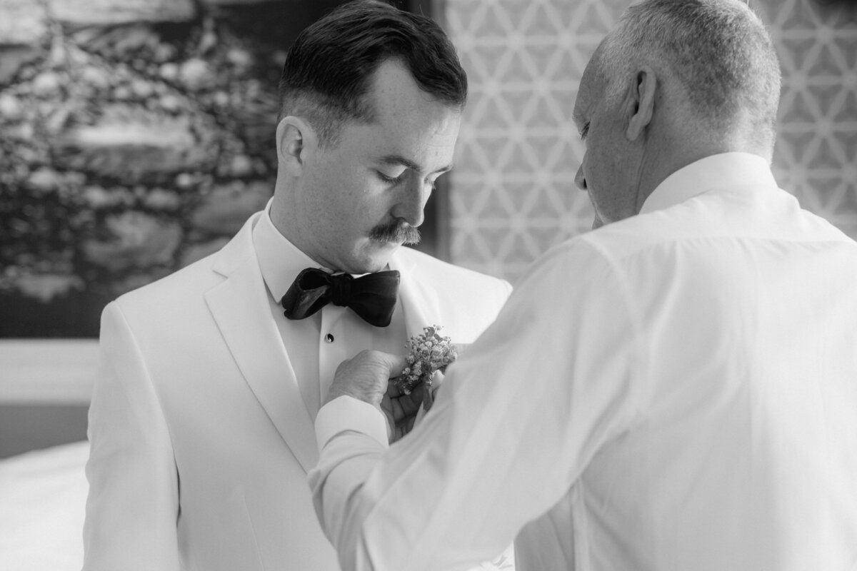 Von seinem Vater bekommt der Bräutigam die Ansteckblume am Revers befestigt.