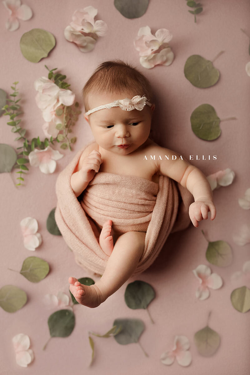 Artistic newborn portrait of baby swaddled in sheets surrounded by leaves