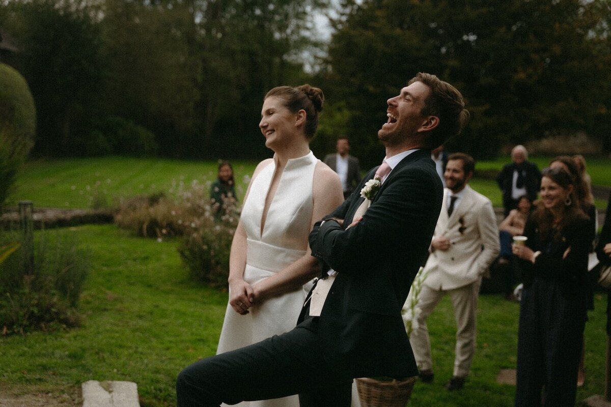 Le marié éclate de rire tandis que la mariée observe une scène, amusée. Une scène saisie par Kamescop, photographe et vidéaste de mariage.