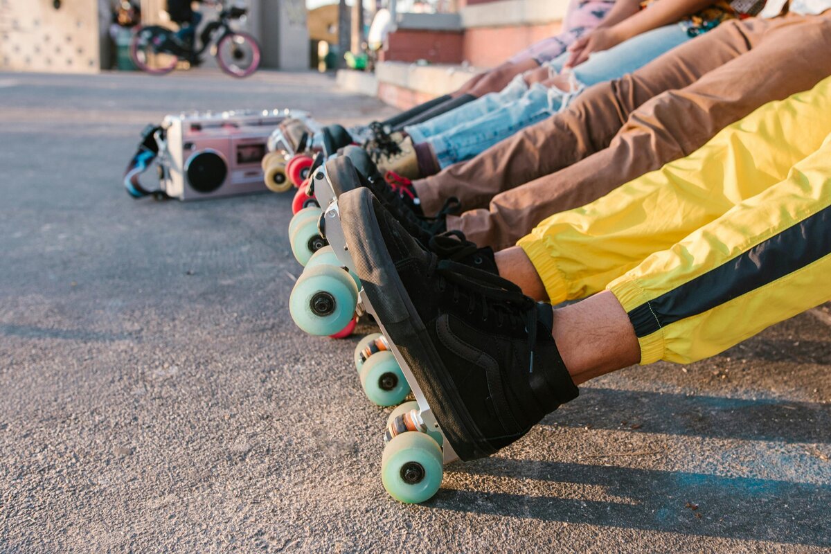 Close-up of people sitting outdoors with skateboards/roller skates and a retro boombox nearby.