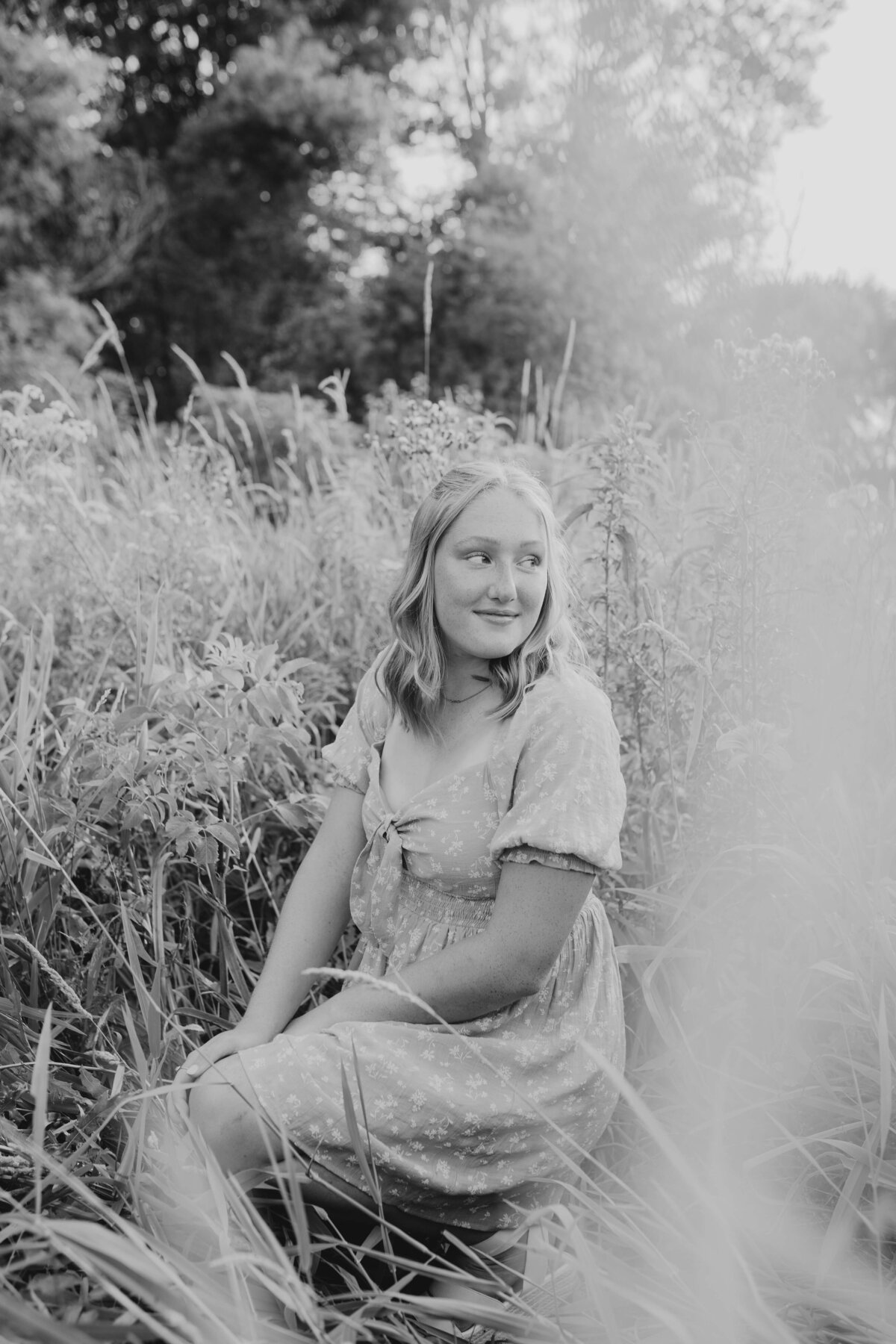 Teen girl sitting in overgrown field, fine art-inspired Michigan senior portraits for grads who want soft, personal storytelling in nature
