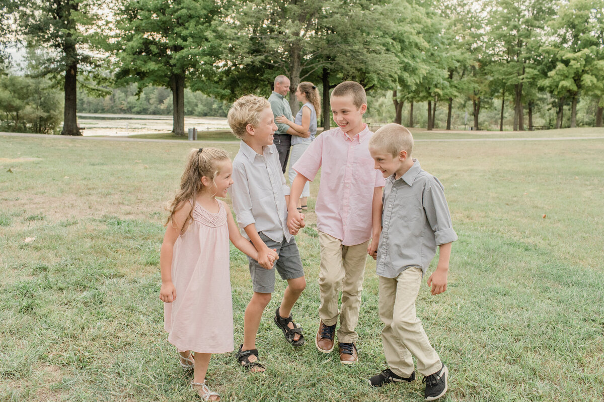 four kids in a park walking and laughing while parents stand in the background