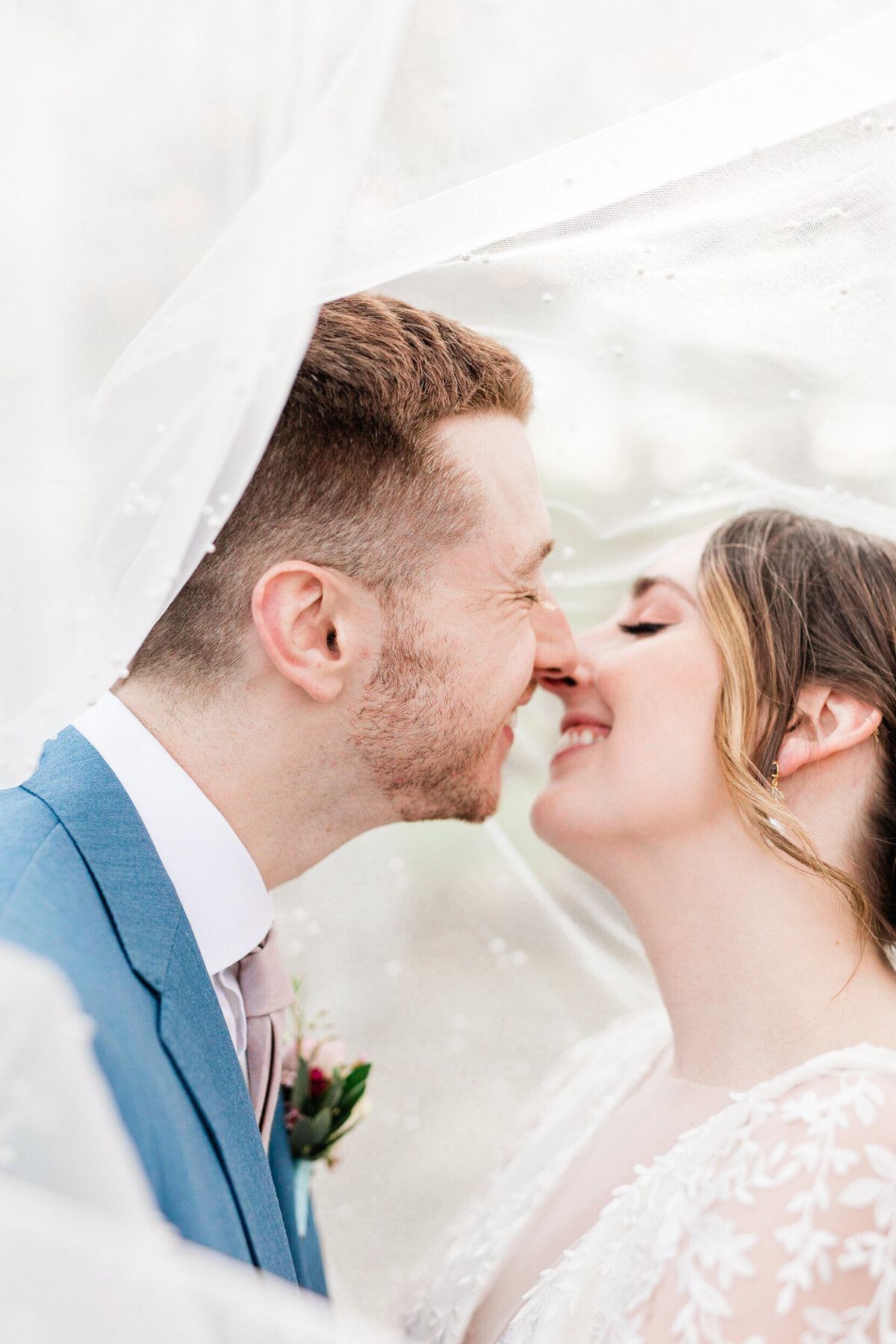 Bride and groom underneath veil about to kiss