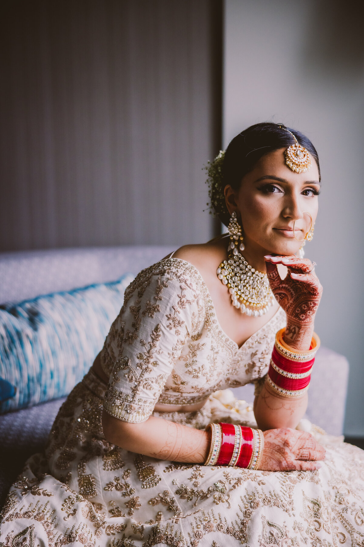 Sikh bride sitting down with her hand under her chin at a hotel in new jersey getting ready before the wedding