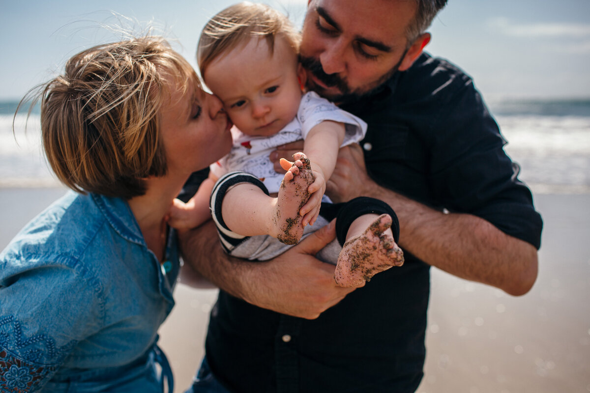 family kiss sandy child on the beach