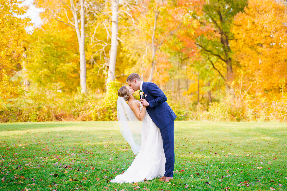 Groom dips his bride and kisses her in front of golden fall leaves at The Pinnacle Gold Course in Grove City, Ohio.