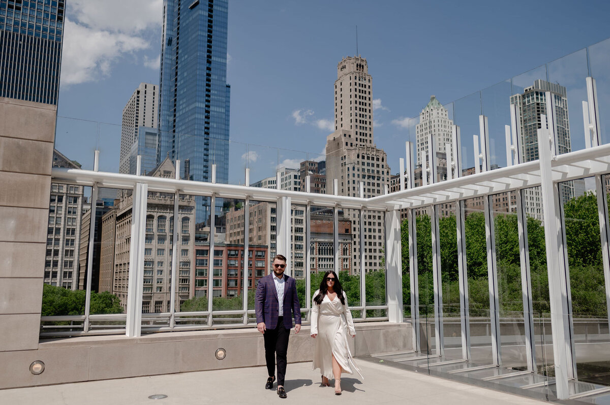 A couple walks on rooftop with Chicago skyline in background.